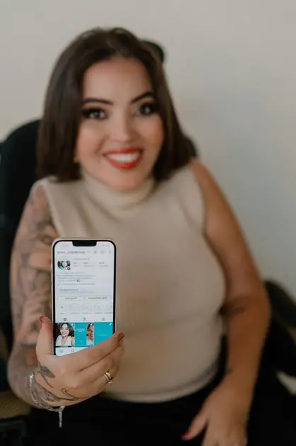 Izabel Broski sorrindo e apresentando seu perfil profissional no celular